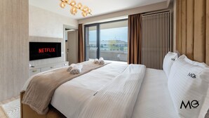 A hotel room with a large bed, a TV displaying 'NETFLIX', a large window with curtains, and a view of buildings outside. - MoHost Valcom - Luxury Skyline Penthouse (Brașov)