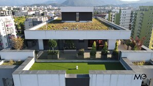 A modern building with a flat roof garden, a central courtyard with artificial grass, and a view of the surrounding cityscape. - MoHost Valcom - Luxury Skyline Penthouse (Brașov)