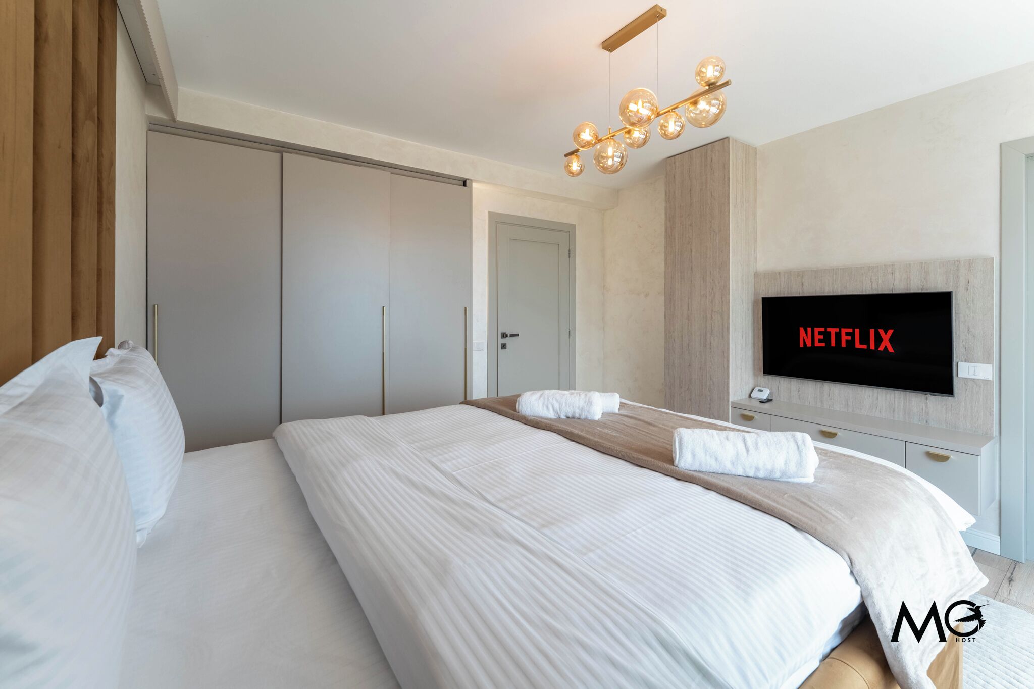 A modern hotel room with a large bed, a television mounted on the wall, and a wardrobe.