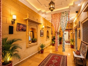 Un pasillo con decoraciones ornamentales en las paredes, plantas en macetas y una alfombra tradicional.