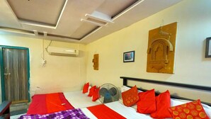 Une chambre d’hôtel avec un lit, un ventilateur sur pied, un climatiseur fixé au mur et une porte.