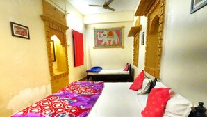 Une chambre à coucher avec un lit, une table de chevet, une couvre-lit à motifs rouges et blancs, un ventilateur de plafond et un mur orné d’un tableau encadré.