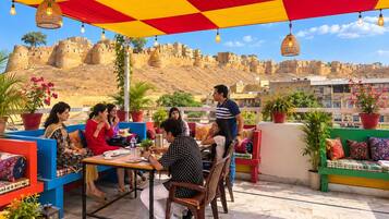 Un grupo de personas cenando en una mesa al aire libre, con una fortaleza histórica al fondo.