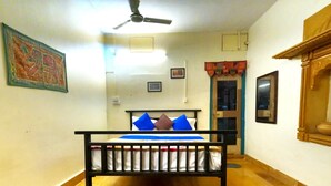 Une pièce avec un lit, un ventilateur de plafond, une porte et un tableau accroché au mur.