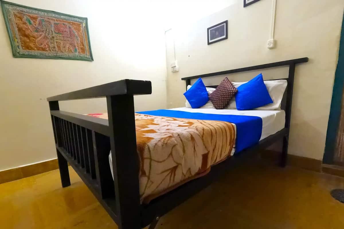 A single bed with a wooden frame, a patterned bedspread, and blue pillows.