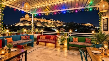 Un espacio al aire libre con varios sofás y mesas, luces colgantes y plantas en macetas.