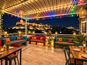 An outdoor seating area with multiple sofas and tables, string lights, and potted plants.