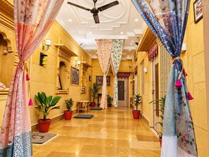 A hotel corridor with a ceiling fan, potted plants, and traditional decor.