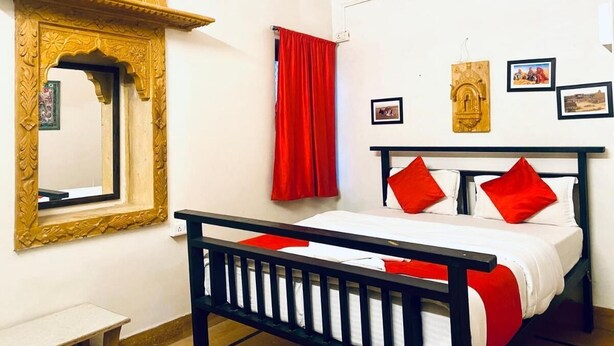 Une chambre à coucher avec un lit, une tête de lit en bois, un rideau rouge, un miroir avec un cadre décoratif et des tableaux accrochés au mur.