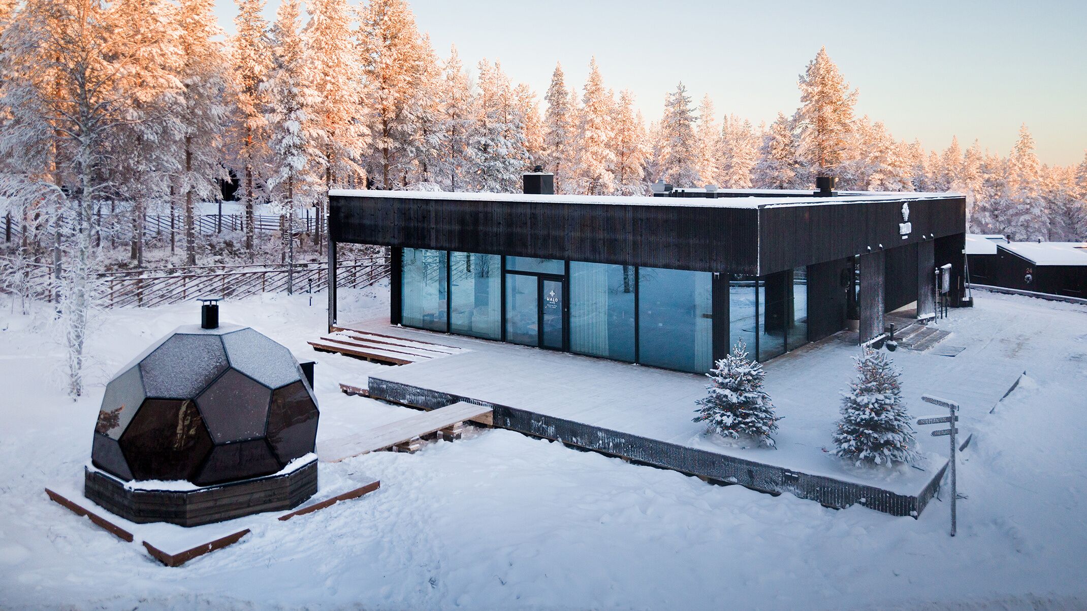 A modern, dark-colored building with large glass windows, surrounded by a snowy landscape and trees.