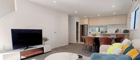 Een moderne woonkamer met een flatscreen televisie, een ronde salontafel en een bank met kleurrijke kussens.