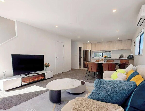 Una sala de estar moderna con un televisor de pantalla plana, una mesa de centro redonda y un sofá con cojines de colores.