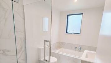 A modern bathroom with a glass shower enclosure, a toilet, a sink, and a bathtub.