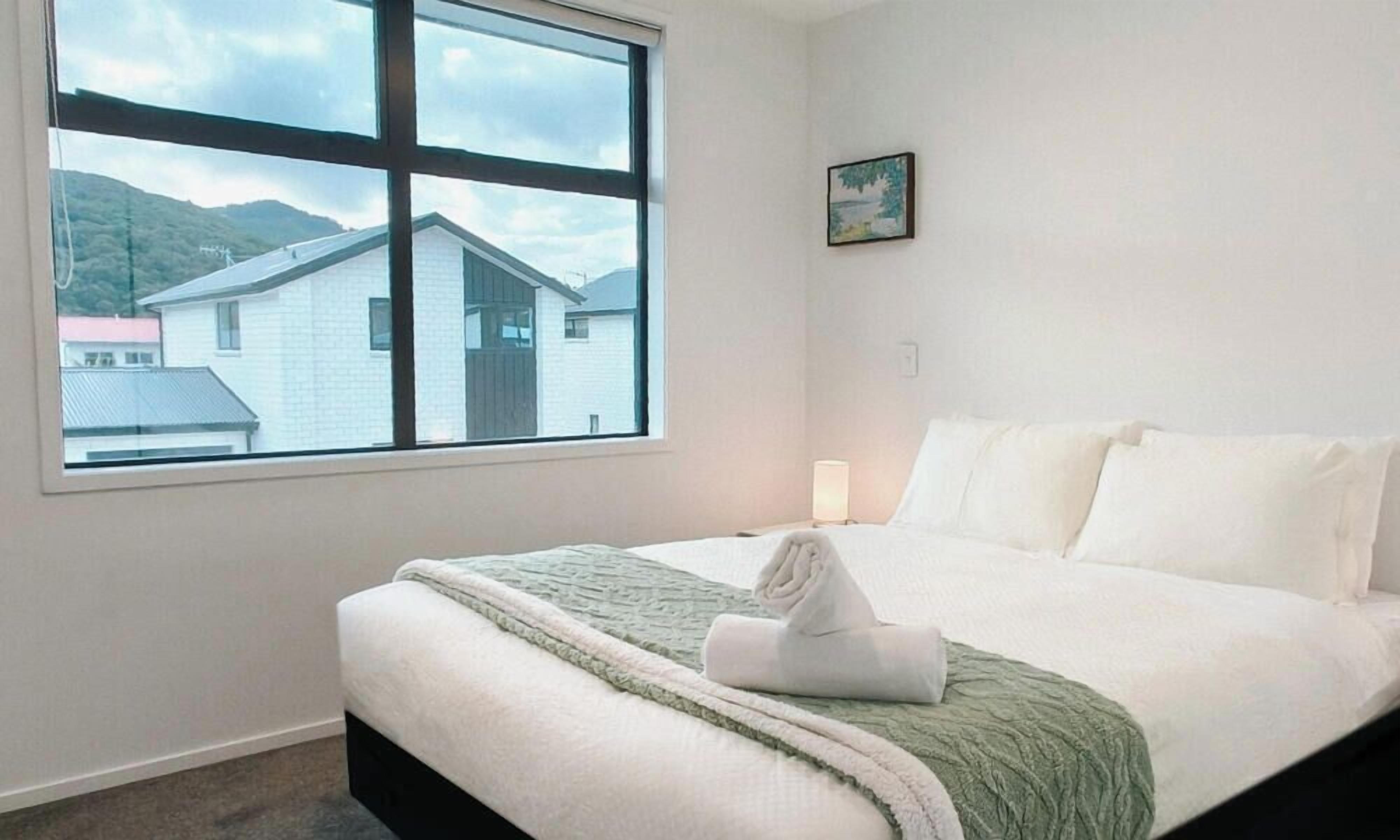 A bedroom with a large window, a bed, a bedside table, and a small picture on the wall.