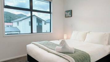 A bedroom with a large window, a bed, a bedside table, and a small picture on the wall.