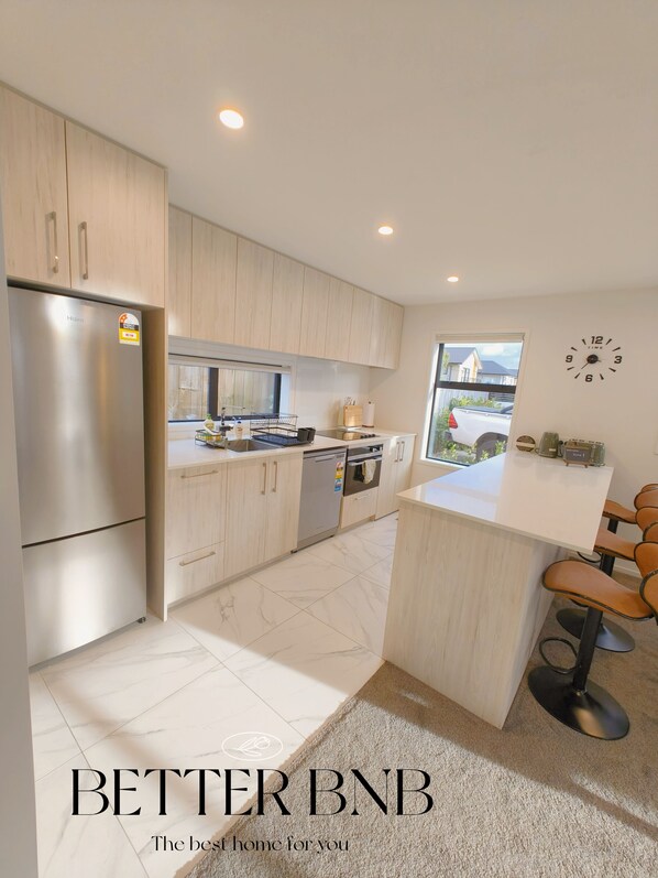 Een moderne keuken met lichte houten kastjes, roestvrijstalen apparatuur en een centraal eiland met barkrukken.