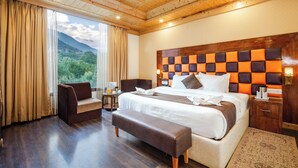 A spacious bedroom with a large bed, a wooden ceiling, a view of greenery outside, and a cozy seating area. - TRIBHAV Rohtang Heights Resort (Manali)