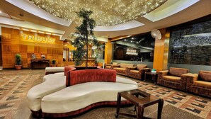 A spacious lobby with a curved sofa, multiple seating areas, a reception desk, and a large tree. - TRIBHAV Rohtang Heights Resort (Manali)