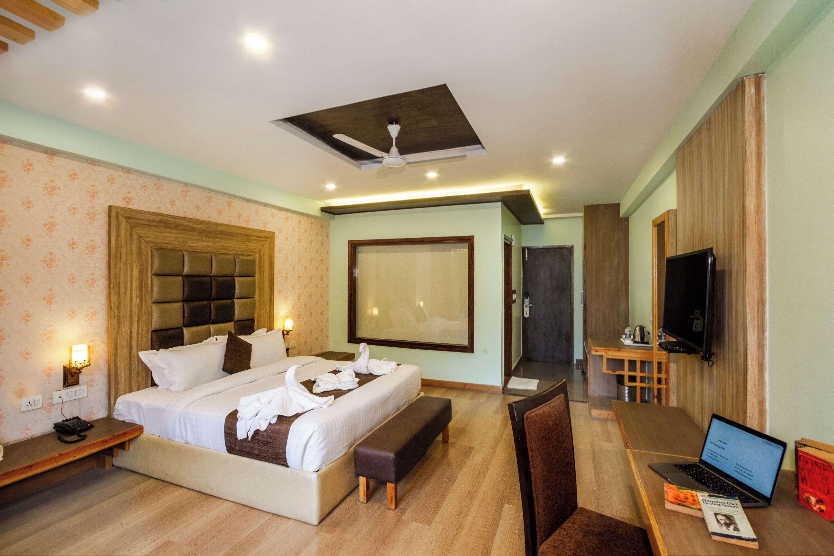 A hotel room with a large bed, a desk with a laptop, a television, and a bathroom visible through an open door.