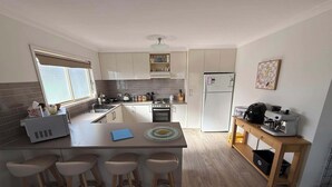 A compact kitchen with a central island, bar stools, a refrigerator, and a coffee machine. - A stylish, family and pet friendly beach retreat near everything! (Cowes)