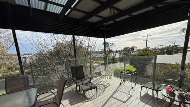 An outdoor deck with a glass balustrade, metal chairs, a table, and potted plants. - A stylish, family and pet friendly beach retreat near everything! (Cowes)