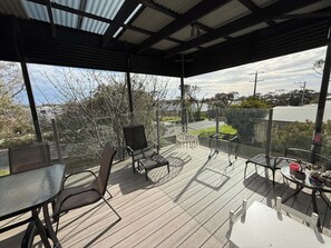 An outdoor deck with a glass balustrade, metal chairs, a table, and potted plants.