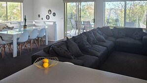 A modern living room with a large sectional sofa, a dining area with a glass table, and a kitchen area with a white countertop. - A stylish, family and pet friendly beach retreat near everything! (Cowes)