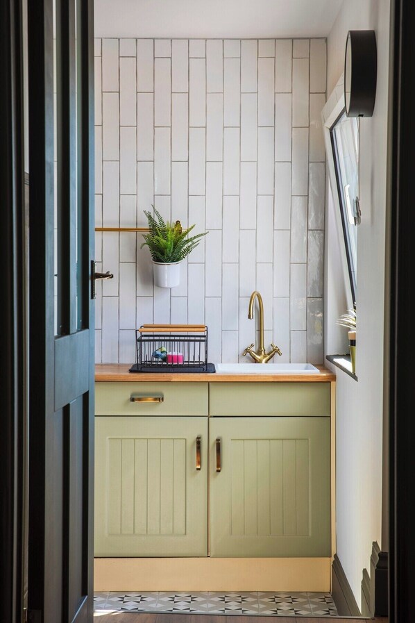 A kitchen with a white tiled backsplash, a green cabinet with a gold faucet, and a small plant on the countertop.