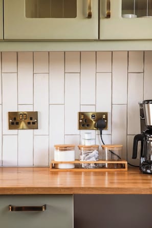 Et køkken med en træbordplade, en kaffemaskine og to lysafbrydere på væggen.