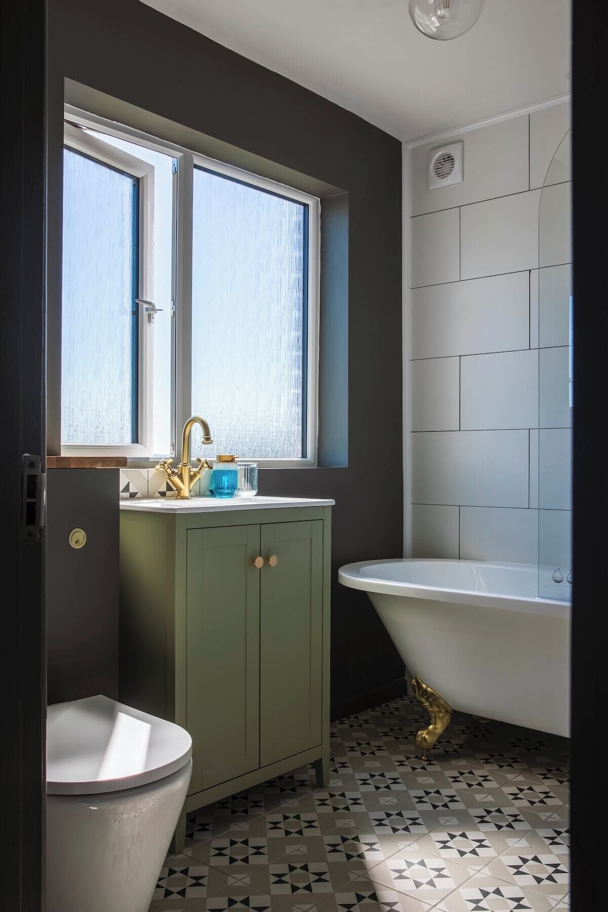 A bathroom with a freestanding bathtub, a window above the sink, and a tiled floor.