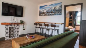 A modern living room with a wooden coffee table, green sofa, and a bar area with bar stools.