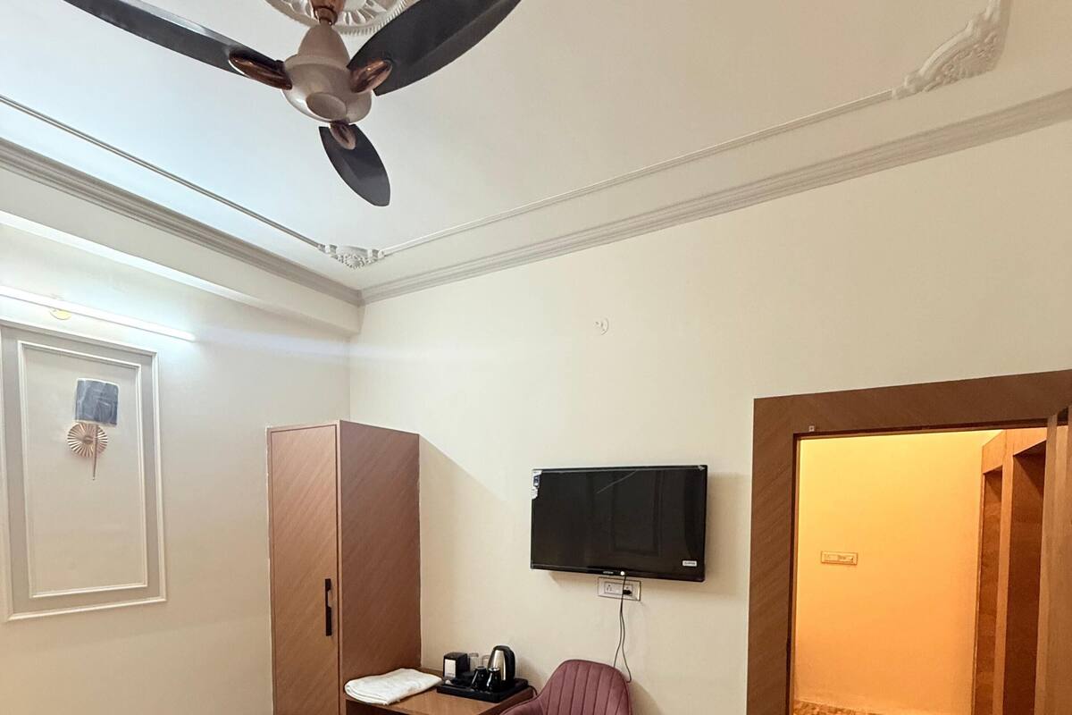 A hotel room with a bed, a desk, a chair, a television, and a ceiling fan.