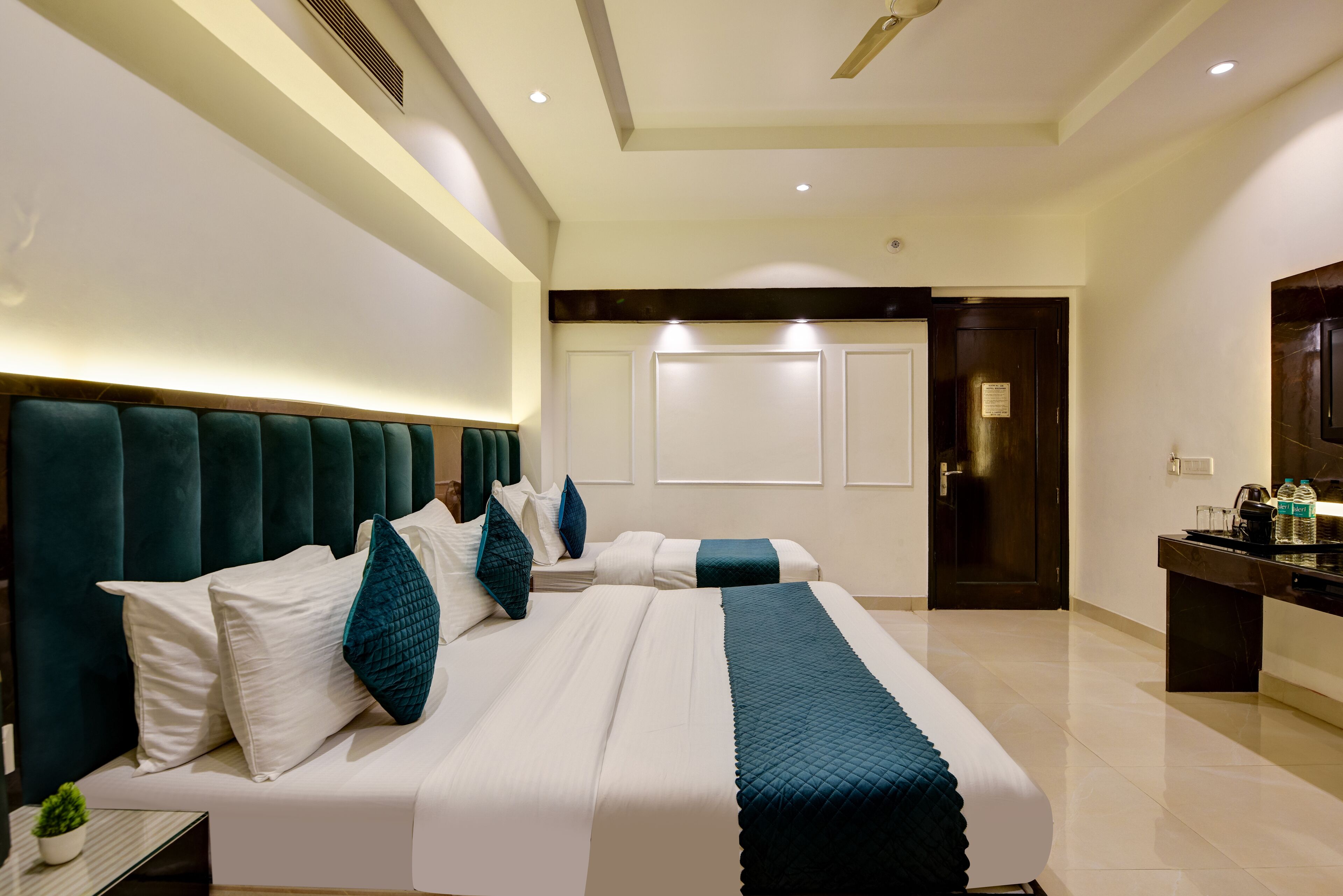 A modern hotel room with a large bed, a bedside table, a small plant, and a dark-toned headboard.