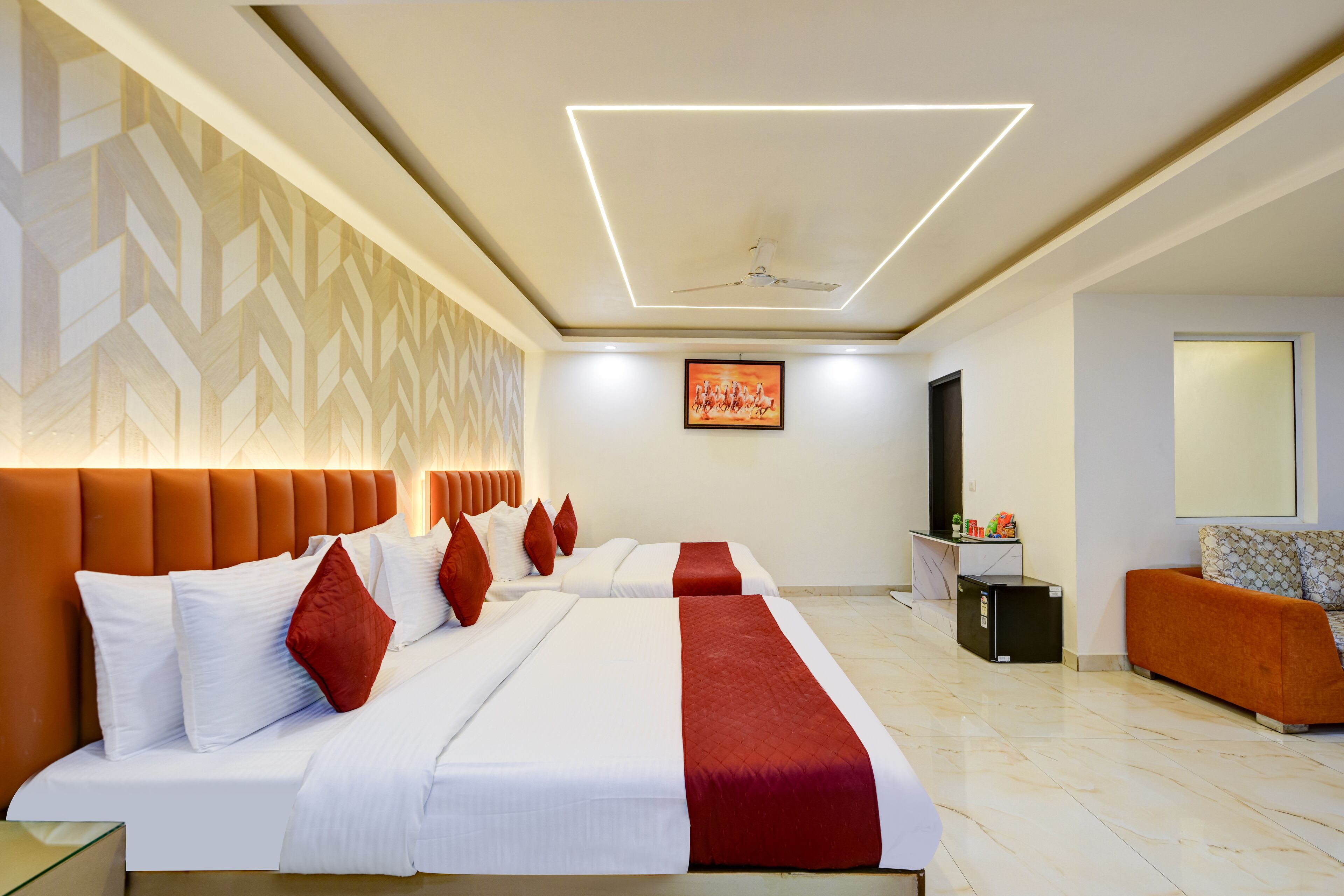 A hotel room with two beds, a sofa, a TV, and a ceiling fan.