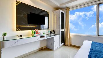 A modern hotel room with a glass desk, a flat-screen TV, a minibar, and a large window with a city view.