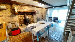 Una cocina rústica con paredes de piedra, una estufa de leña, una mesa con sillas y vistas al exterior.