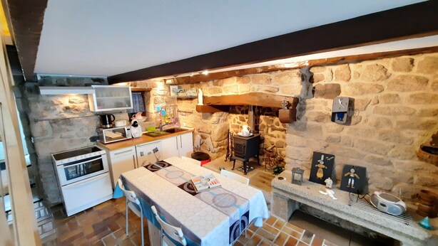 Una cocina compacta con pared de piedra, estufa integrada, microondas y un pequeño comedor.