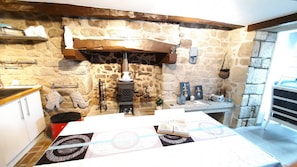A rustic kitchen with stone walls, a wooden countertop, and a built-in wood stove.