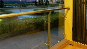 A balcony with a glass railing overlooking a building and a landscaped area.