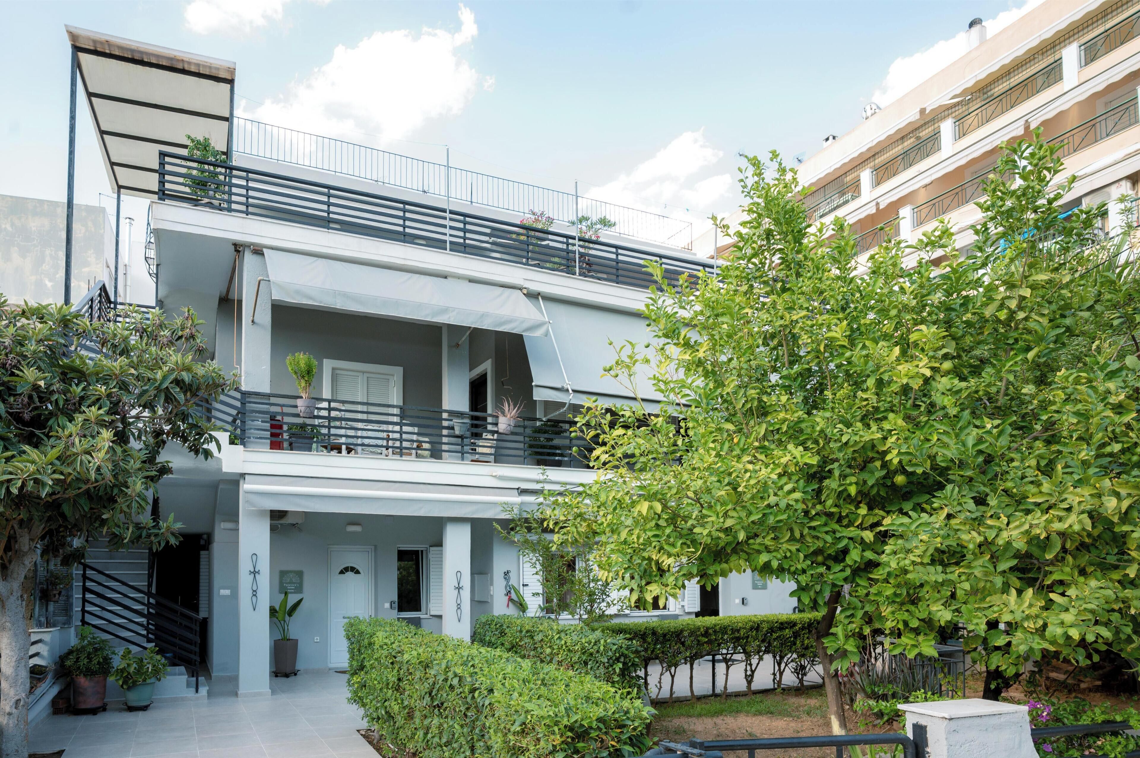 Un edificio moderno de dos pisos con balcón, plantas en macetas y un jardín bien cuidado.