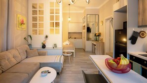 A modern living room with a sofa, a dining table, and a kitchen area with a refrigerator and cabinets. - Peacock's Apartments (Moschato-Tavros)