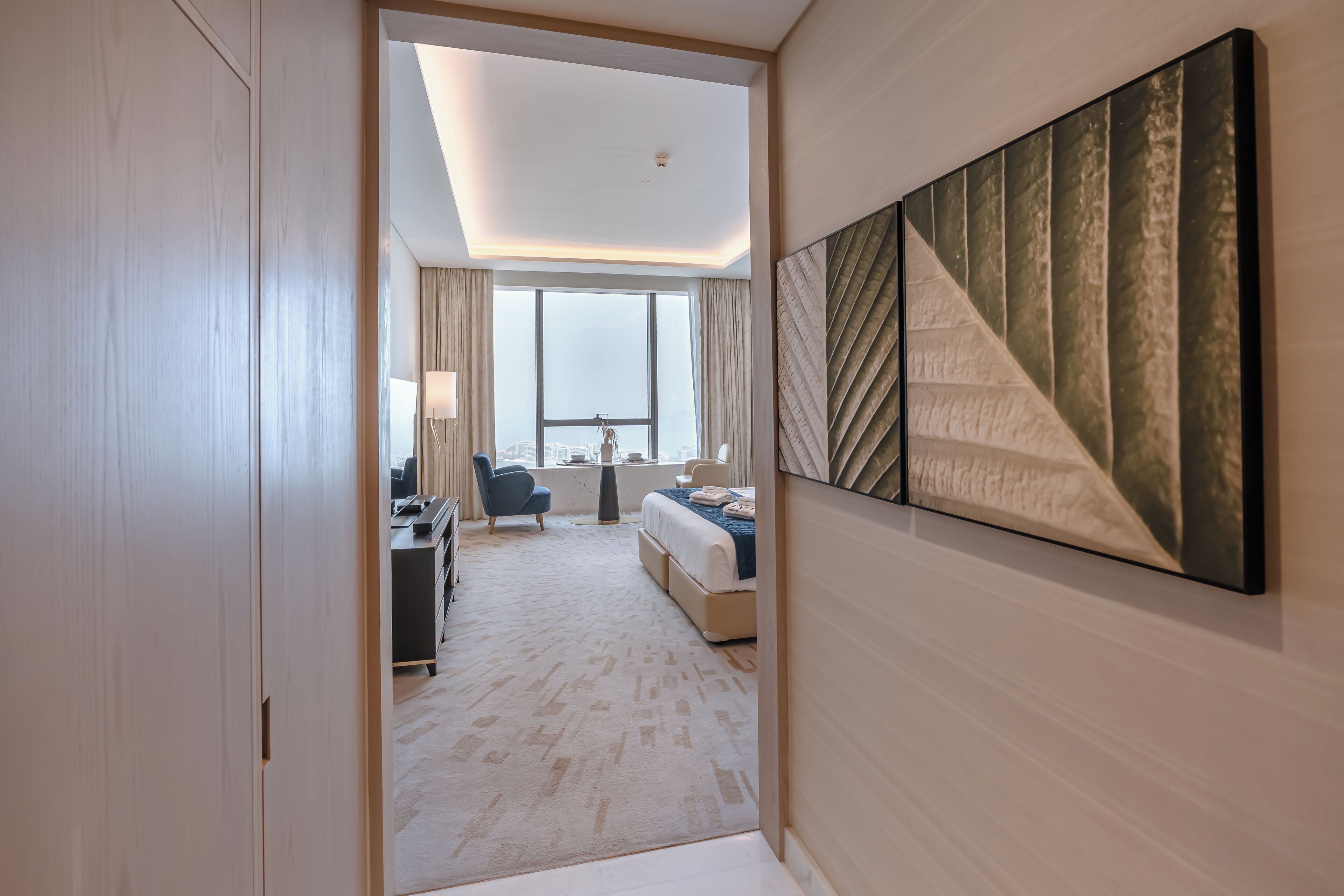 Habitación de hotel moderna con una cama grande, un escritorio, una silla y vistas a la ciudad a través de amplios ventanales.