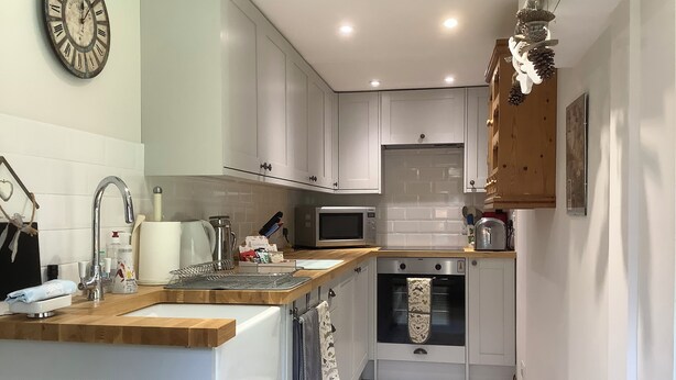 A modern kitchen with white cabinets, a wooden countertop, a built-in oven, and a wall-mounted clock.