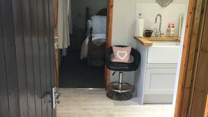 A compact room with a wooden door, a small stool with a heart-shaped cushion, a white sink, and a bed with a wooden headboard.