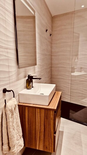 Un baño moderno con un espejo grande, un lavabo blanco y muebles de madera.