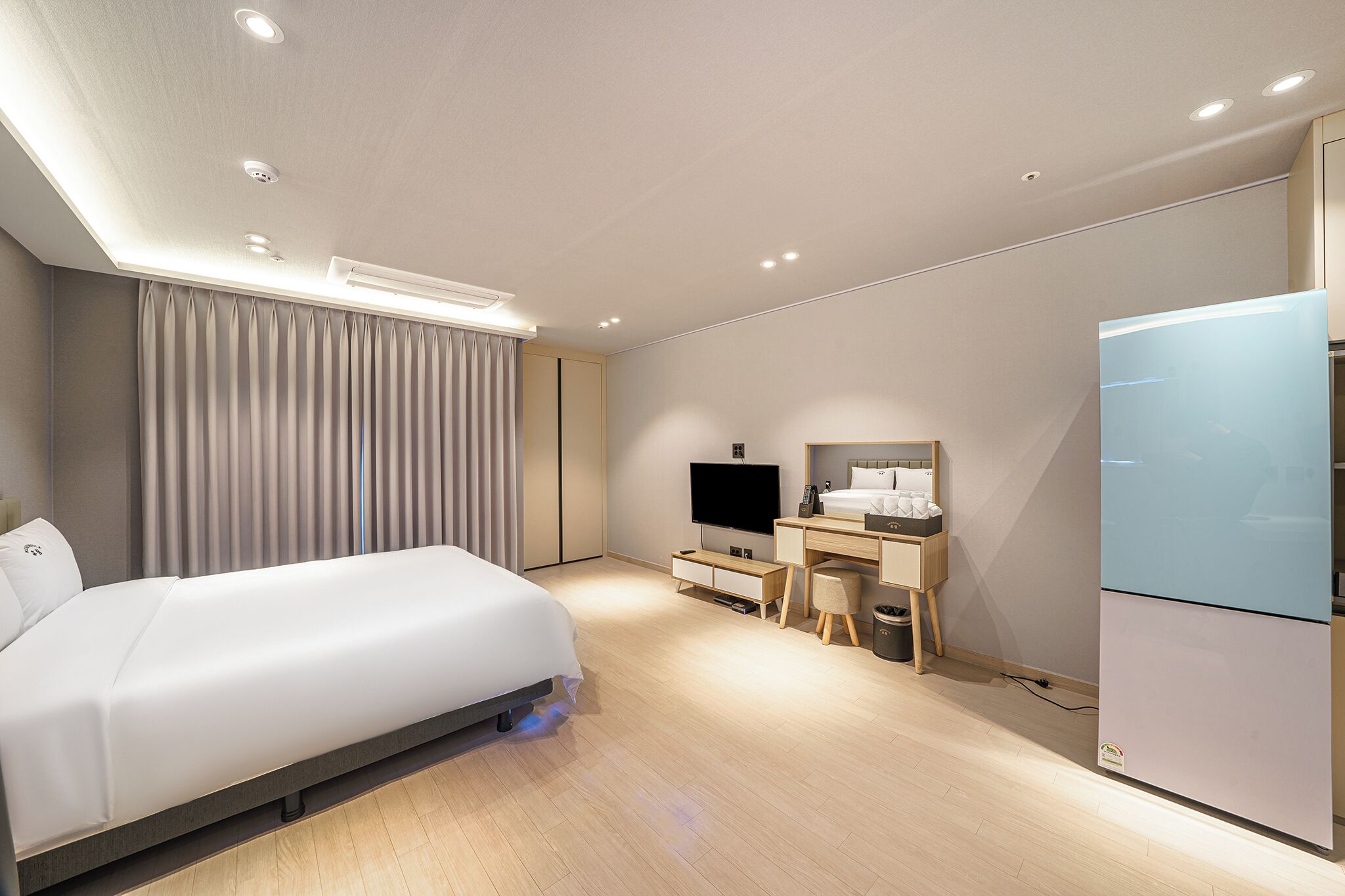 Een moderne hotelkamer met een bed, een televisie, een bureau met een spiegel en een koelkast.