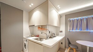 A compact kitchen with a built-in washing machine, a sink, and a small dining area with a table and chair. - JIncheon hotel hue (Jincheon)