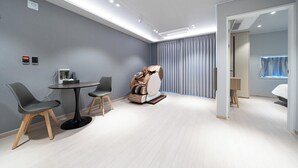 A modern room with a massage chair, a small round table with chairs, and a large window with curtains. - JIncheon hotel hue (Jincheon)