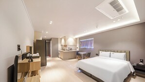 A modern hotel room with a large bed, a desk with a mirror, a small kitchen area, and a bathroom. - JIncheon hotel hue (Jincheon)