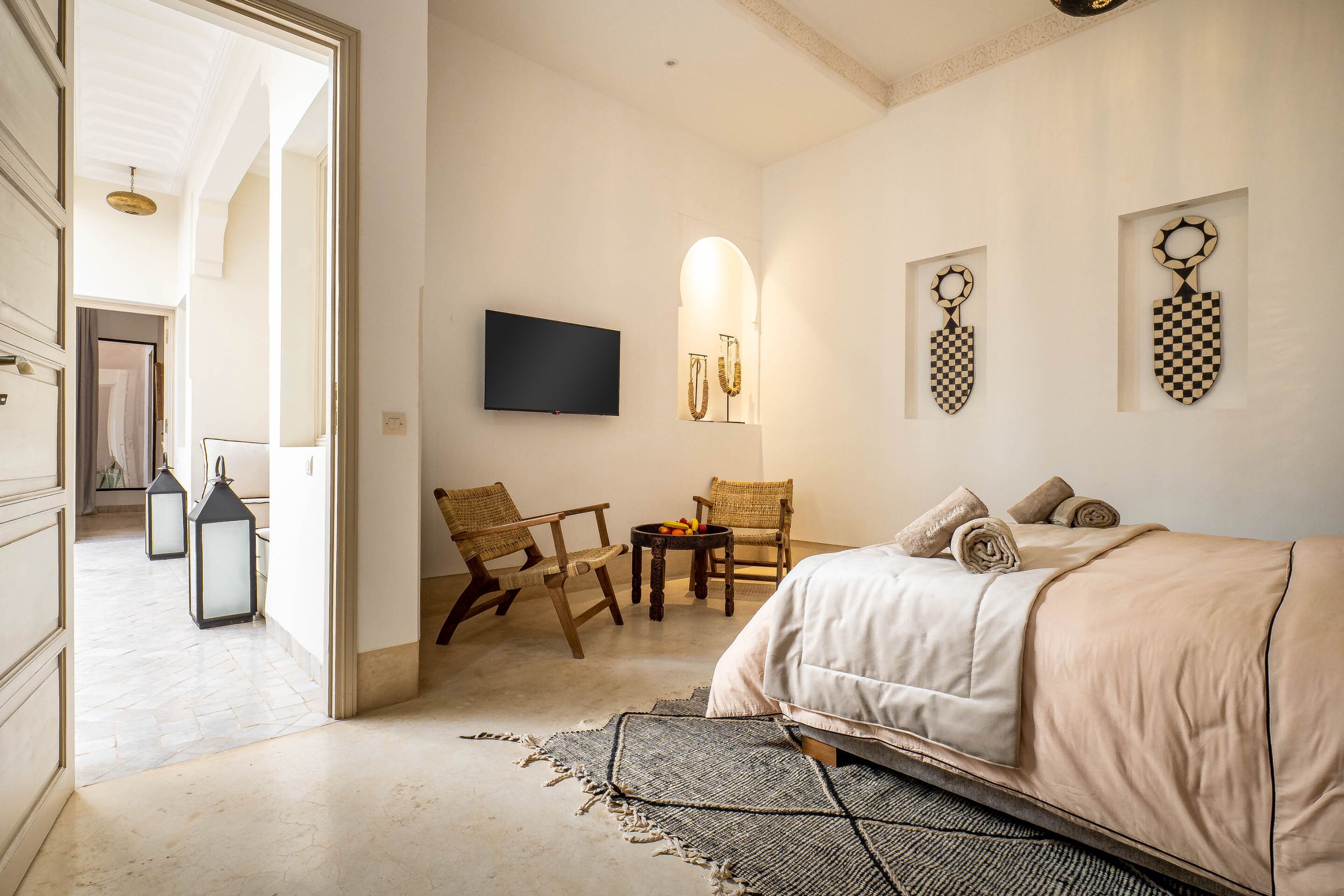 A bedroom with a bed, two wicker chairs, a small table with fruit, and wall-mounted decor.